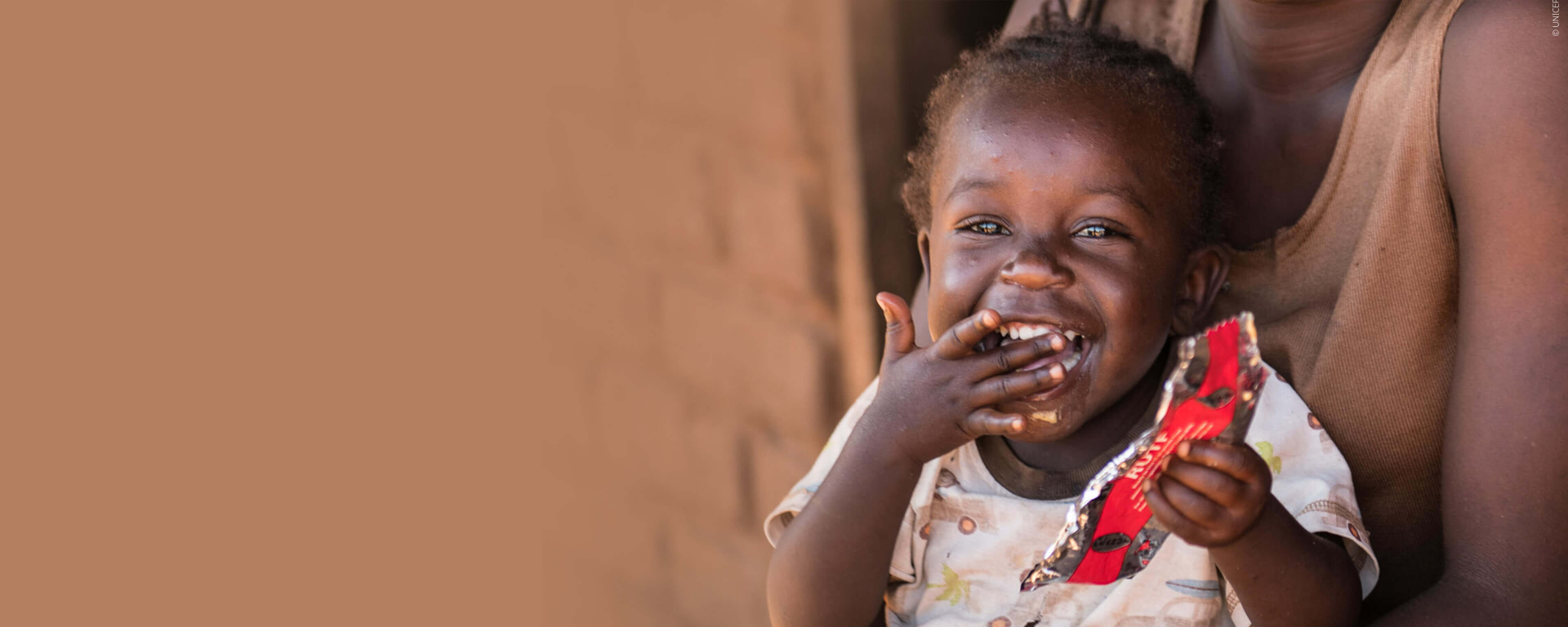 Małe roześmiane dziecko w trakcie otrzymywania pomocy od UNICEF w postaci terapii pastą odżywczą RUTF.