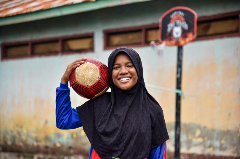 Uśmiechnięta Tia pozuje z piłką do futsalu na podwórku szkolnym w Larantuka