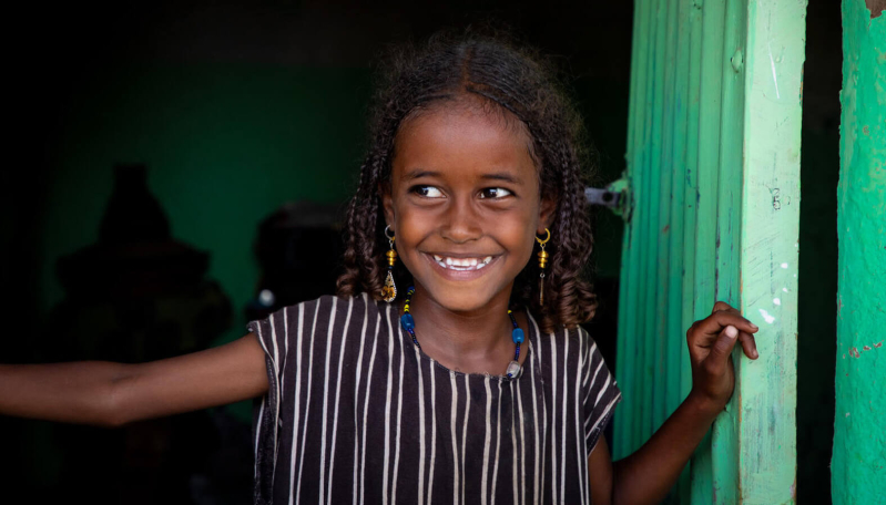 Siedmioletnia Kedo uśmiecha się, patrząc przez drzwi. Jej marzeniem jest zostać lekarzem.