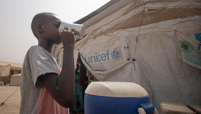 Ali pije wodę przy namiocie UNICEF