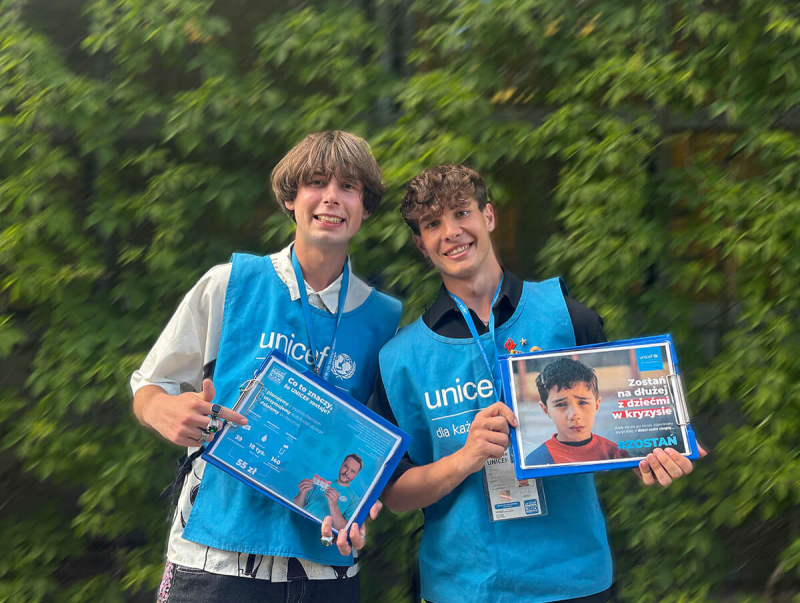 Fundraiserzy ubrani w niebieskie kamizelki z logo UNICEF trzymają broszury m&oacute;wiące o misji organizacji.