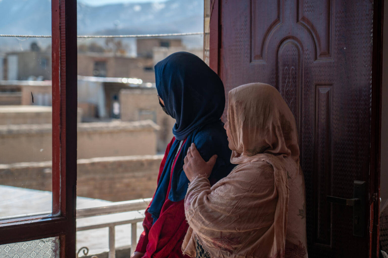 14-letnia Wahida ze smutkiem patrzy przez okno, a jej mama stara się pocieszyć c&oacute;rkę.
