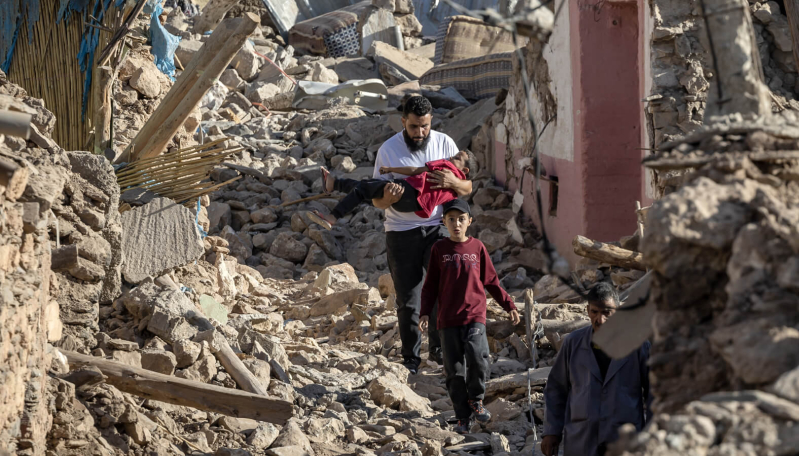 Maroko: mężczyzna niesie dziecko przez ruiny