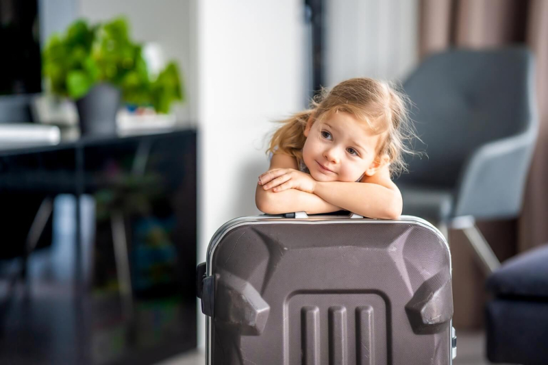Uśmiechnięta dziewczynka opiera się na walizce, czekając na zameldowanie w hotelu.