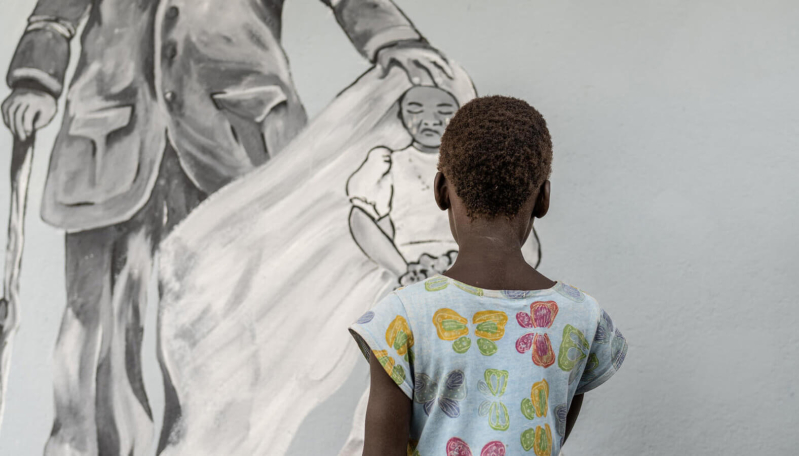 Dziewczynka stoi przed muralem przedstawiającym płaczące dziecko w welonie ślubnym.