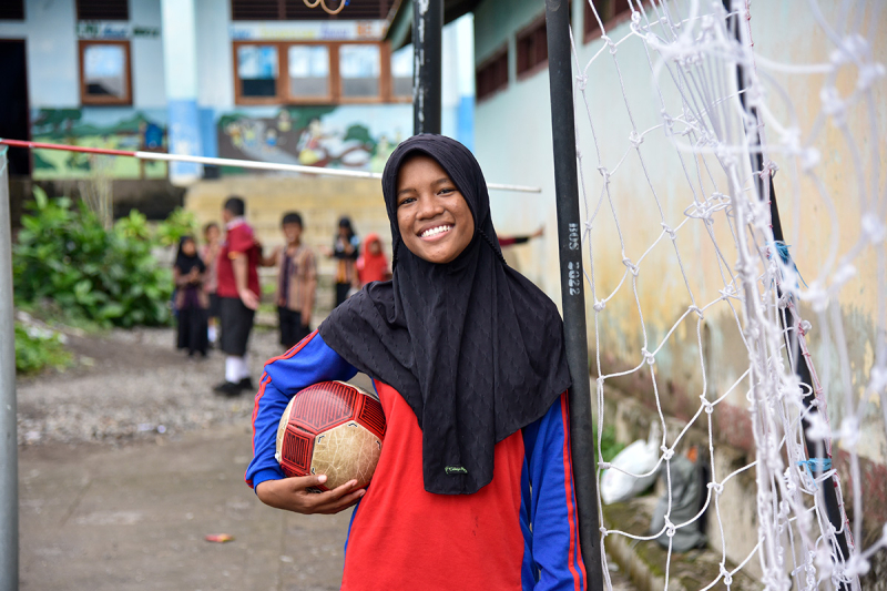 Uśmiechnięta Tia pozuje z piłką do futsalu na podwórku szkolnym w Larantuka.
