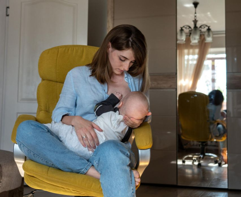 Kobieta siedzi na żółtym fotelu i karmi dziecko piersią