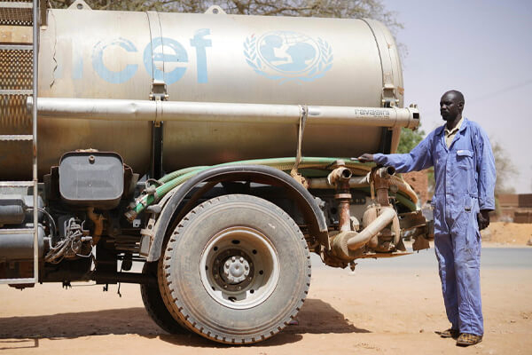Kierowca na tle cysterny z wodą z logo UNICEF