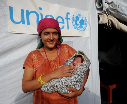 kobieta trzymająca na rękach dziecko, stojąca przed namiotem UNICEF